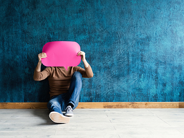 young man holding pink paper speech bubble in front of his head, leaning against a blackboard